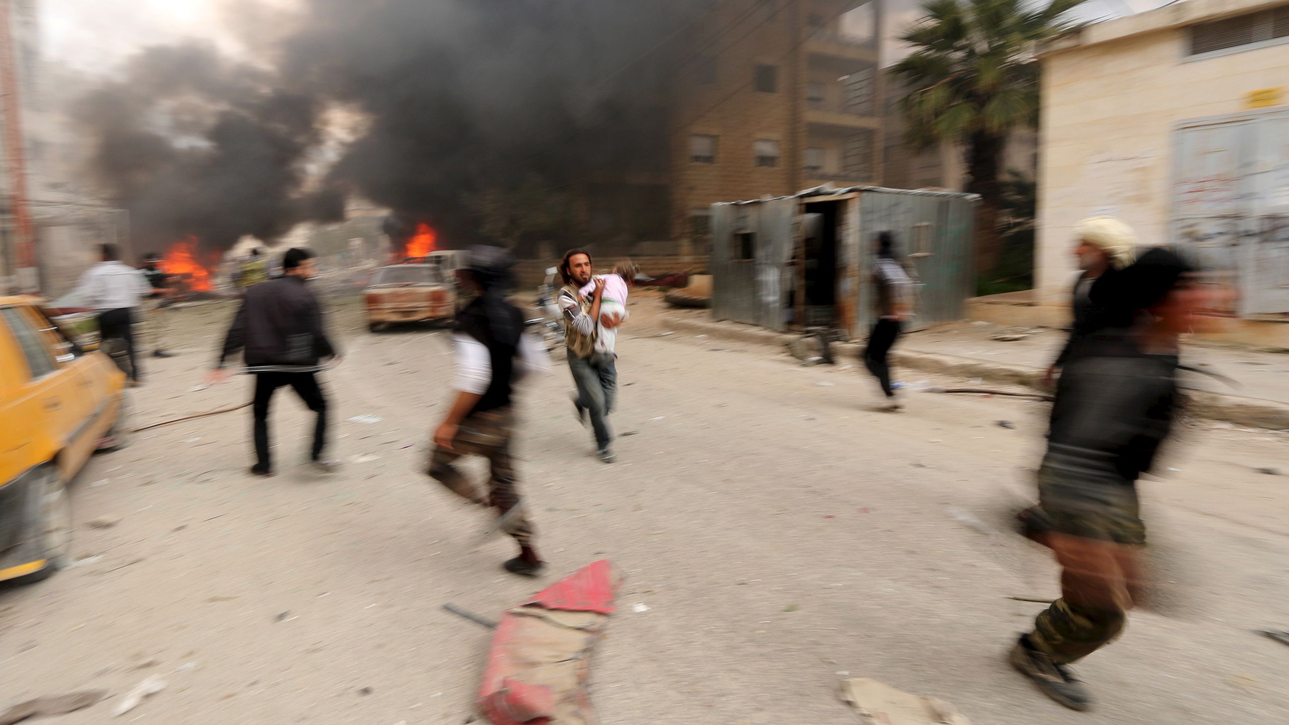 En mann løper med et skadet barn etter bombing i Idlib i 2015.